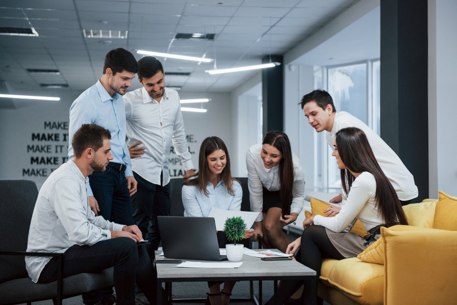 Group of young professionals collaborating around a laptop in a modern office meeting space.